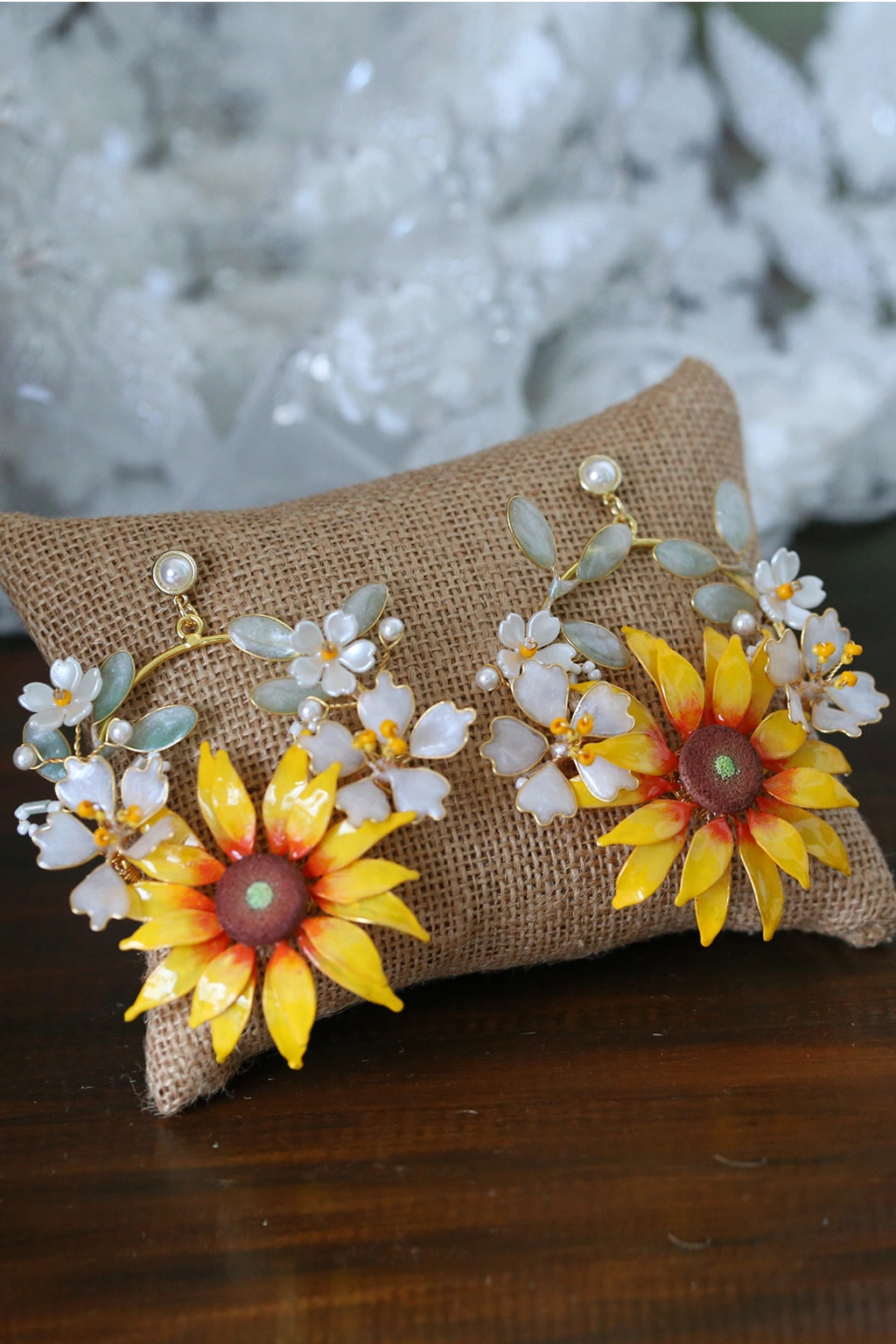 Handcrafted resin sunflower earrings with yellow and orange petals, white flower accents, green resin leaves and pearls on a jute cushion, perfect for bridal haldi or mehndi.