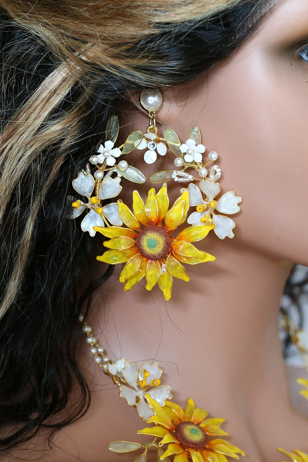 Close up of a woman wearing handcrafted resin sunflower earrings with yellow and orange petals, white flower accents, green resin leaves and pearls, perfect for bridal haldi or mehndi.
