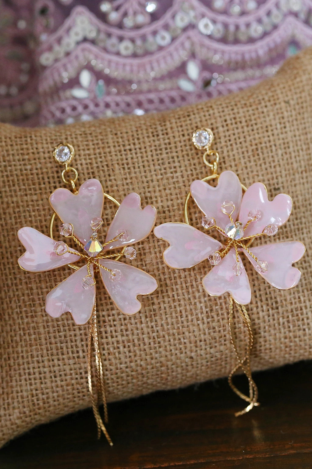 Handmade blush pink resin flower earrings made with gold plated wire and crystal accents displayed on a jute cushion, perfect for bridal wear and festive occasions.