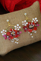 Handcrafted resin flower earrings in shades of red, blush pink, and ivory with pearl detailing and gold accents, displayed on a rustic jute background — lightweight bridal jewelry.