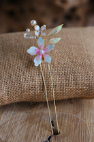 Handmade resin floral bridal hair pin with pastel petals, pearls and gold detailing styled on natural fabric background